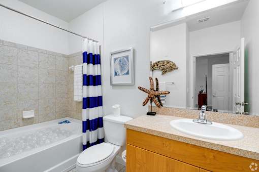 A bathroom with a white toilet, a white sink, a white bathtub, a blue and white striped shower curtain, a starfish decoration, and a mirror.