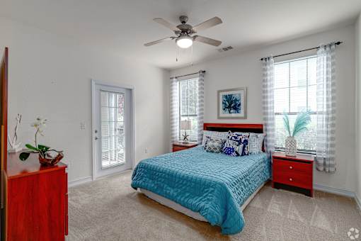 A bedroom with a blue bedspread and a ceiling fan.