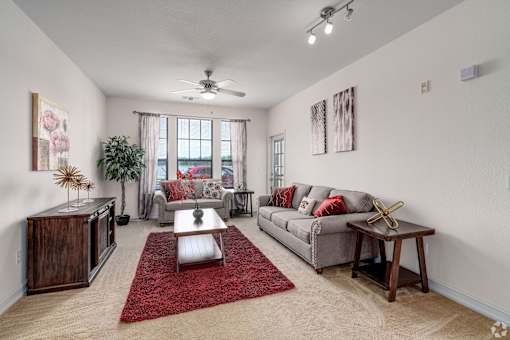 A living room with a grey couch, a red rug, and a ceiling fan.