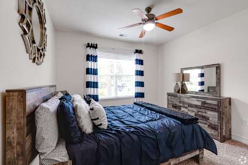 A bedroom with a bed, dresser, mirror, and a ceiling fan.