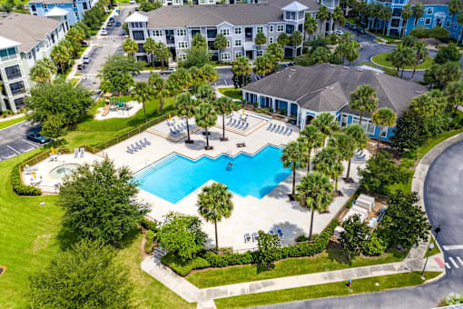 An aerial view of a swimming pool surrounded by palm trees and a building.