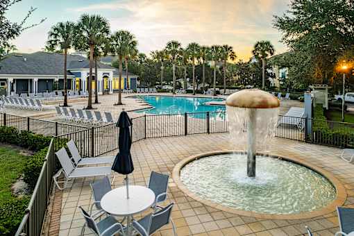 A pool area with a fountain, chairs, and umbrellas.