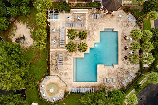 An aerial view of a swimming pool surrounded by trees and a patio area.
