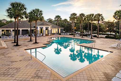 A pool surrounded by palm trees and a building in the background.