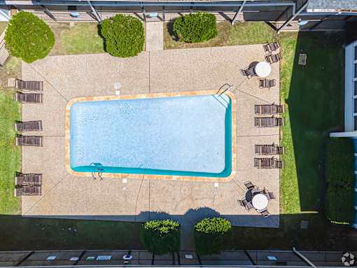 An aerial view of a swimming pool surrounded by a concrete patio and a grassy area.