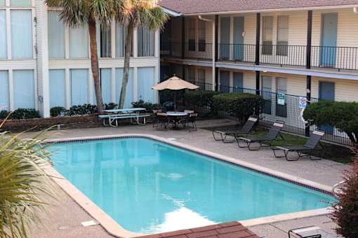 A pool surrounded by chairs and a building with blue doors.