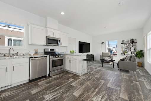 the living room and kitchen of a home with white cabinets and stainless steel appliances