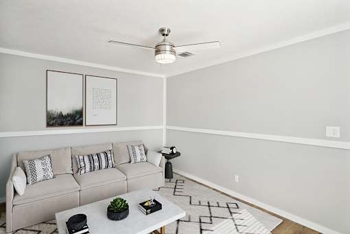 A living room with a grey couch, a white coffee table, and a ceiling fan.