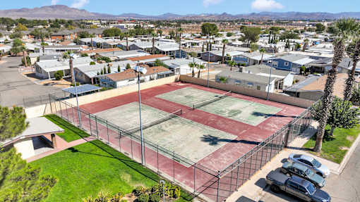 A tennis court is surrounded by a fence and a parking lot.