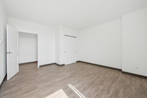 A room with white walls and wooden flooring with a rug in the middle.
