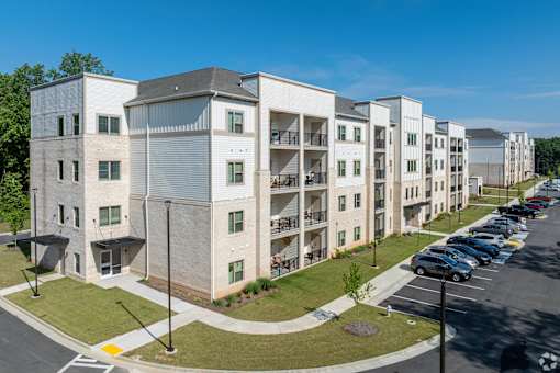 A row of modern apartment buildings with cars parked in the lot.