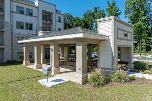A small white building with a porch is in front of a multi-story apartment building.