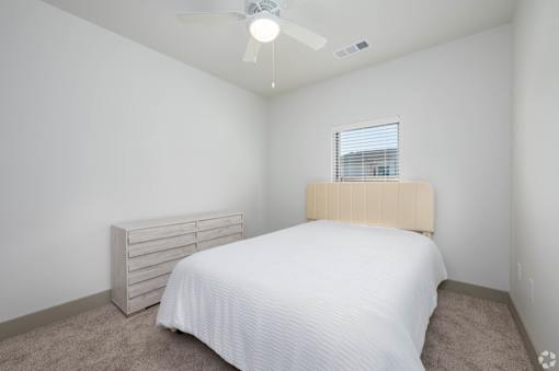A bedroom with a bed, a window, and a fan.