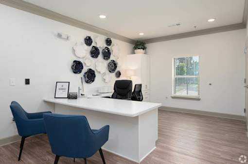 A white reception desk with a blue chair and a white wall with a black and white decoration.