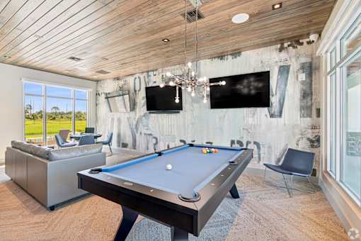 A pool table is in the middle of a room with a tv and a chair.