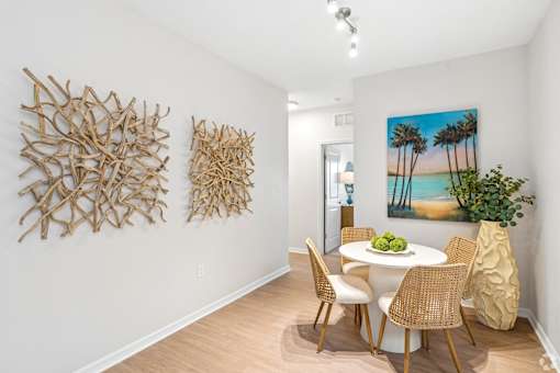 A dining room with a white table and chairs, a painting of a beach scene, and two pieces of artwork on the wall.