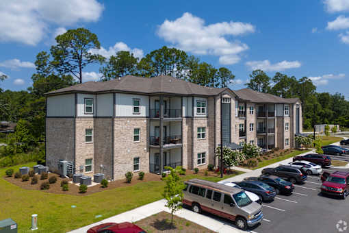A parking lot in front of a building with a red car in the foreground. at Arbours at Kingsland, Georgia, 31548