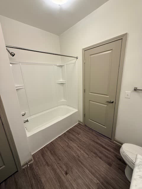 A white bathtub with a shower head is in a bathroom with a toilet and a door.