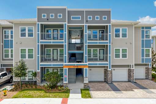 A modern apartment building with a grey and blue exterior and a red and white striped awning.