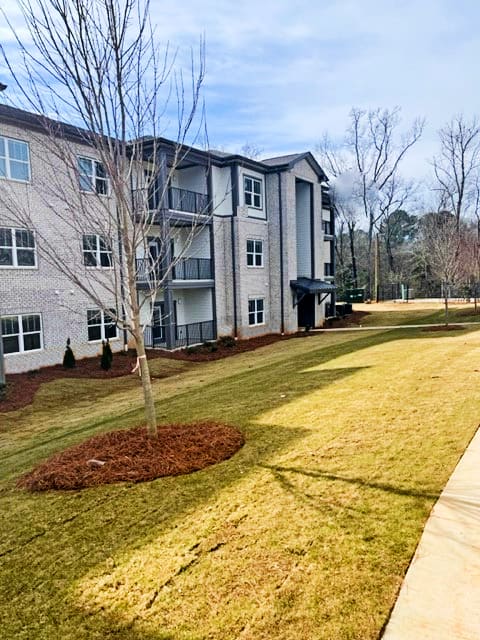 A tree in a mulched bed in front of a building at Arbours at Covington Apartments, Covington, GA, 30014