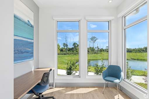 A room with a desk, chair and a view of a field and trees.