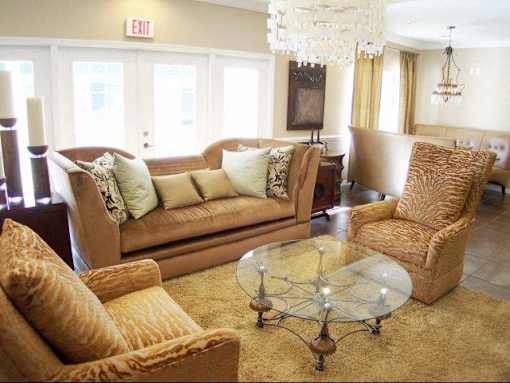 A living room with a tan couch, a glass coffee table, and a chandelier at Arbours at Ensley Apartments, Pensacola, 32514