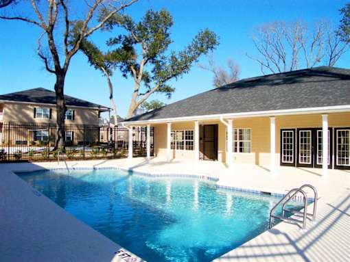 A swimming pool in front of a house with a tree at Arbours at Ensley Apartments, Pensacola