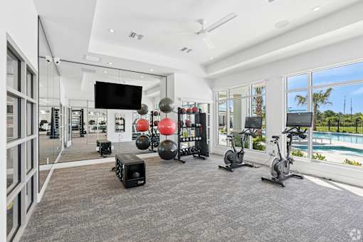A spacious gym with a variety of exercise equipment and a view of the pool outside.