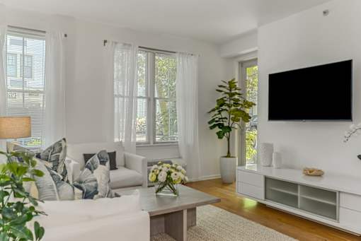 A living room with a white couch, a wooden coffee table, and a large flat-screen TV mounted on the wall.