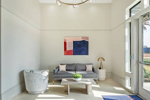 A modern living room with a grey couch, a grey armchair, a wooden coffee table, and a large abstract painting on the wall at The Addison,Louisiana 70836