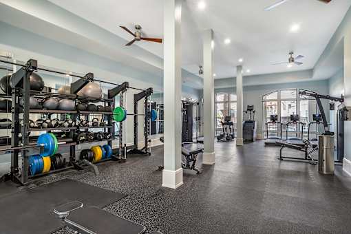 A gym with a variety of equipment including weight plates, weightlifting equipment, and a bench press at The Addison, Baton Rouge, Louisiana