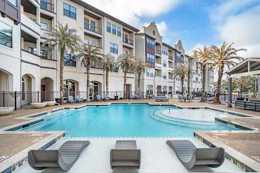 A swimming pool surrounded by lounge chairs and palm trees in front of a multi-story apartment building at The Addison, Baton Rouge, LA