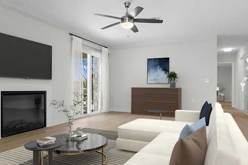 A modern living room with a white sofa, a coffee table, a flat screen TV, and a ceiling fan.