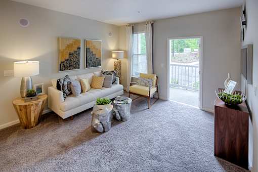 A living room with a couch, two chairs, and a table with a vase on it at Capital Creek at Heritage Apartments, Wake Forest