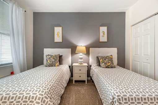 two twin beds in a bedroom with grey walls and a window at Pier Village Apartments, Long Branch, 07740