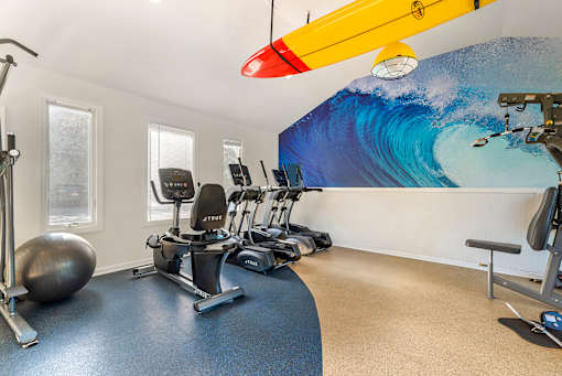 a gym with exercise machines and a surfboard on the wall at Quail Ridge, Plainsboro Township, 08536