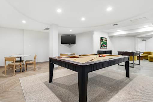 A billiard table is in the middle of a room with a TV mounted on the wall.