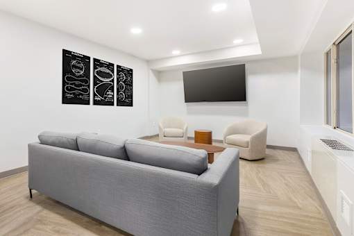A grey couch sits in a living room with a television and two chairs.