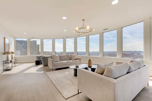 A large, well-lit living room with a view of the cityscape outside the windows.