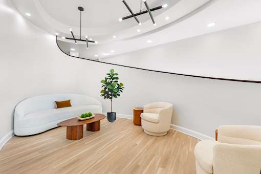 A living room with a white couch, a wooden coffee table, a potted plant, and two chairs.