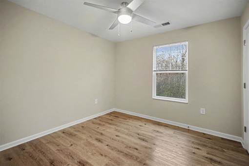 A room with a ceiling fan and a window with a view of trees.