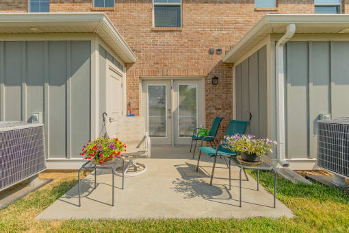 a patio with two chairs and two tables in front of a brick building