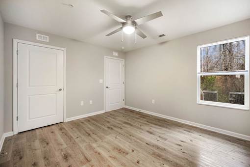 A room with a ceiling fan and a window showing trees outside.
