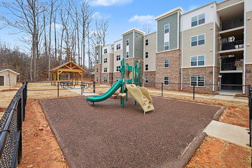 A playground with a green slide in front of apartment buildings.