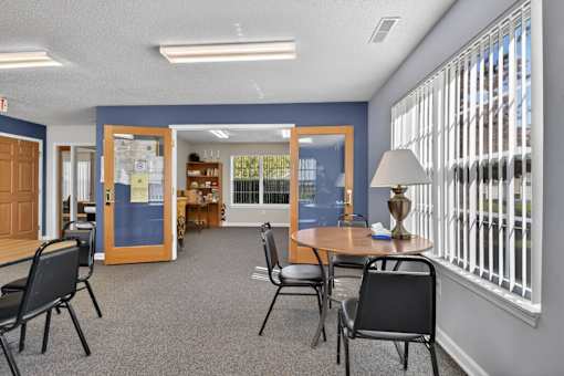 A room with a table and chairs in front of a window with blinds.