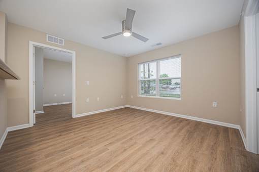 A room with a ceiling fan and a window with a view of trees and a house.
