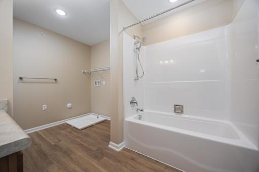 A white bathtub with a shower head and a white mat on the floor.
