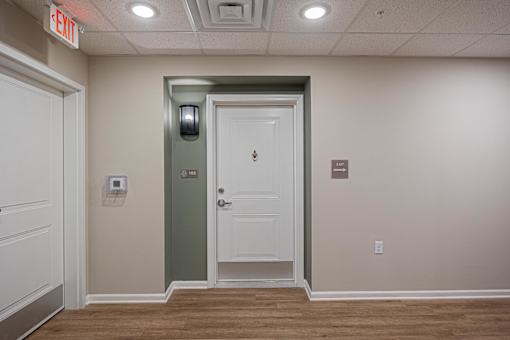 A white door with a green frame is in a room with a red exit sign above it.