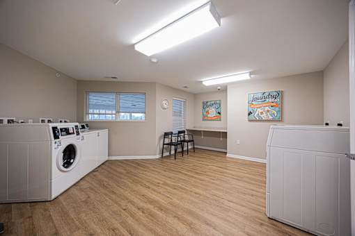 A laundry room with a washer and dryer, a chair, and two paintings on the wall.