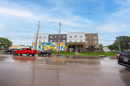 A red car is parked in front of a building with a colorful mural on the side.